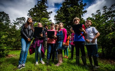 A group of children stand in a bunch with clipboards looking thoughtful.