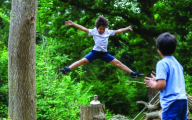 Children star jumping with trees behind 