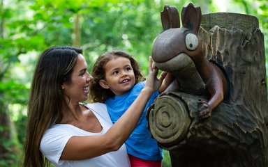 A woman holds her young daughter up to a sculpture of the squirrel from the gruffalo story