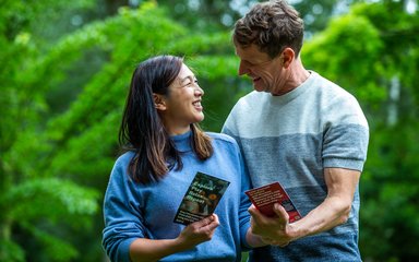 A husband and wife smile at each other holding a Friends of Westonbirt Arboretum leaflet in their hands