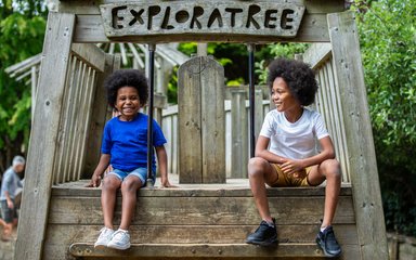 2 young boys sit on a wooden playing feature smiling to the camera