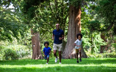 Man and two boys running on grass surrounded by trees