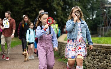 2 young girls walk holding magnifying glasses to their eyes.