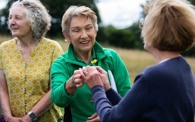 A volunteer in green holds a wildflower for a visitor to admire