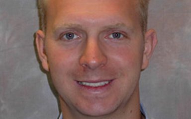 A man with short blonde hair and blue eyes smiles at the camera