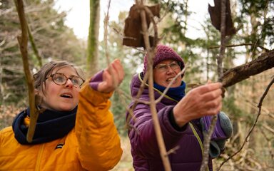Close-up of two women smiling as they examine a tree branch.