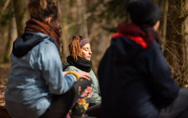 A woman sitting with eyes closed on the forest floor.