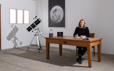 woman sat at desk with telescope beside