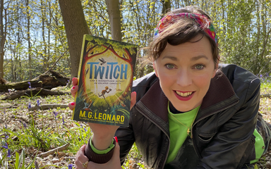 A woman with brown hair tied back with a red headband lies on the floor of a forest with a book in her hand called Twitch