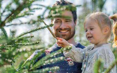 dad and young daughter smiling at a Christmas tree