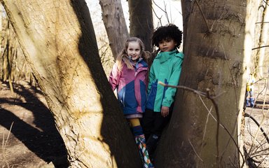 Two children in coats standing within a tree