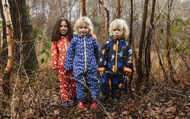 Three children stand in a forest