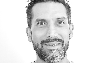a black and white photo of a man with dark hair and beard smiling at the camera