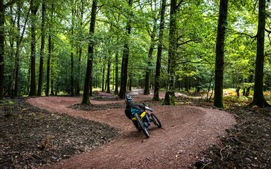A man riding a three wheeled adapted bike along a mountain bike trail in a forest