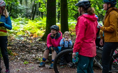 A group of female mountain bike riders sitting and laughing with a young girl