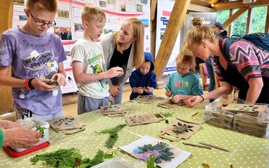 A family stand around a table of crafts. The adults help the children with the craft they are making