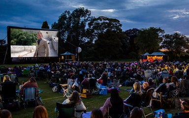 A crowd gather in the forest to watch an outdoor cinema screening of No Time To Die