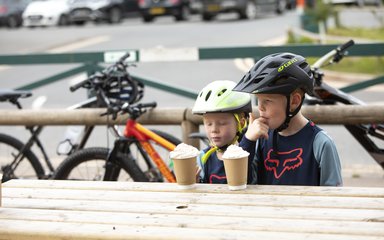 Two children enjoying a hot chocolate with bikes in the background
