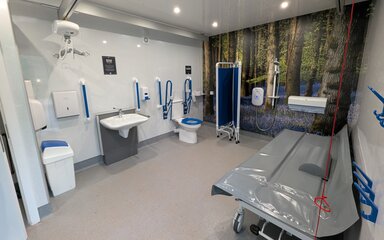 The inside of a Changing Places facility which includes a toilet, hoist, shower, privacy screen and adult changing table.