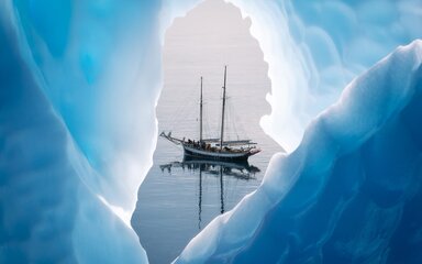 A tall ship with sails down, seen through a gap among ice bergs.