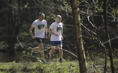 Two men running through the woods on a trail