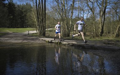 Two men running across stepping stones in a river in the woods 