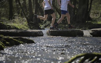 two runners crossing a stream on a running trail in the forest