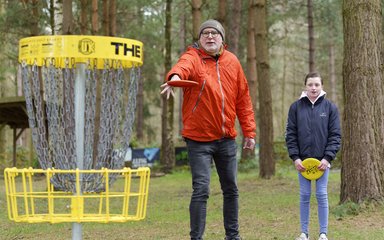 Old bearded man in a green woolly hat and female child playing disc golf