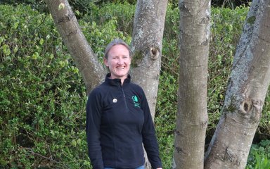 Member of staff Sarah Wood smiling against a backdrop of trees