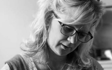 A black and white photo of a woman with light hair wearing glasses looking down