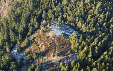 A drone shot looking down on a frosty hill top surrounded by coniferous trees