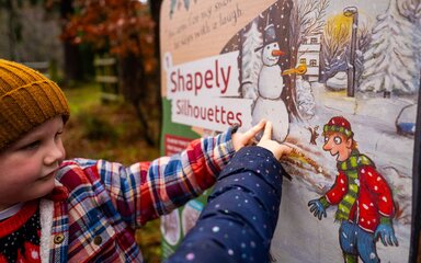 Two children pointing at a Christmas-themed display panel in the forest.