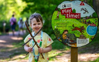 A smiling girl holding a stick figure standing next to a Stick Man themed sign that says 'play time'