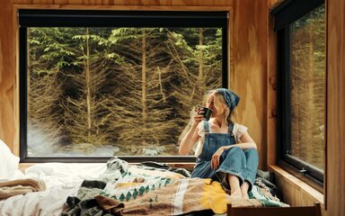 A woman sat drinking a drink on a bed in a cabin
