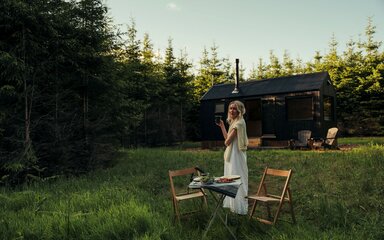 A woman stood outside of a cabin with a dinner set up