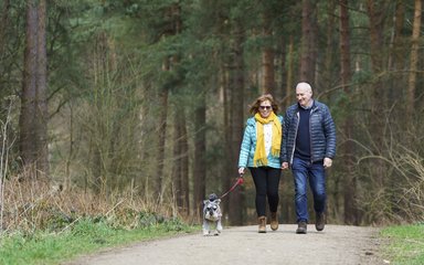 A man and a woman walking on a trail with their small dog on a lead