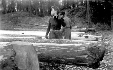 Black and white image of a Lumberjill standing next to a recently felled tree