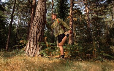 A man leaning against a tree in the forest as he stretches.
