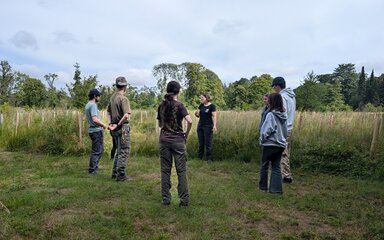 A group of young people circle round a Westonbirt employee to learn about tree care.