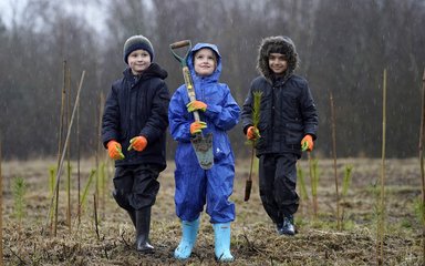 three children planting trees on a rainy day