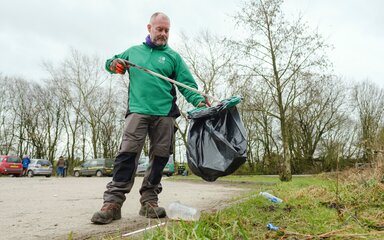 A man in Forestry England uniform litter-picking on a grass verge.