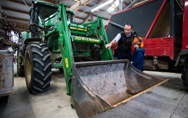 A dad and young boy stand by a large tractor peering. 