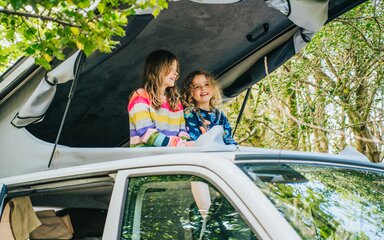Two girls at the top of a pop top in a campervan