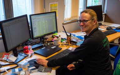 A woman wearing Forestry England branded clothing sits at a busy work desk.
