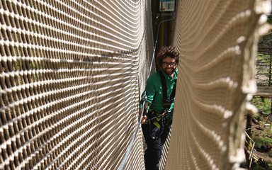 A man smiling whilst travelling through a treetop rope bridge with net sides