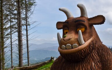 A close up of a Gruffalo sculpture with trees and mountain views behind