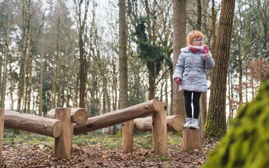 A young girl in winter coat and gloves in a forest play area.