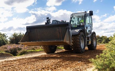 A tractor with a bucket on the front spreading gravel on a track to smooth out the surface.