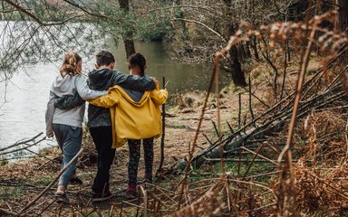 Three children walking together arm in arm, next to a lake