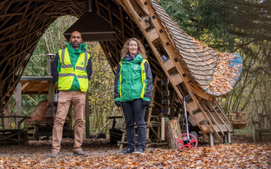 Two people in forestry work uniforms standing under a wooden arch in a forest